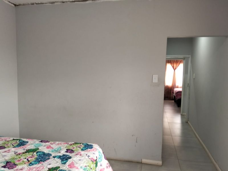 A bedroom interior featuring tiled flooring and a doorway leading to an adjacent room, showing signs of wear on the walls and ceiling.