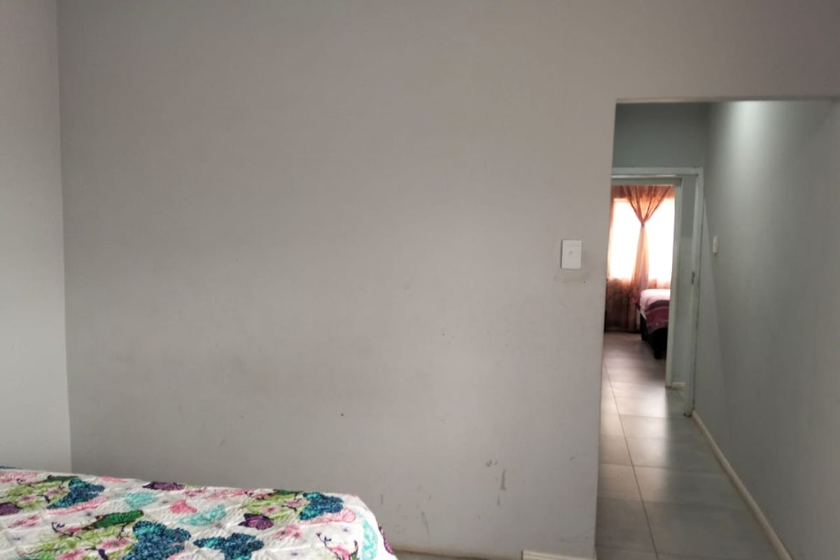 A bedroom interior featuring tiled flooring and a doorway leading to an adjacent room, showing signs of wear on the walls and ceiling.