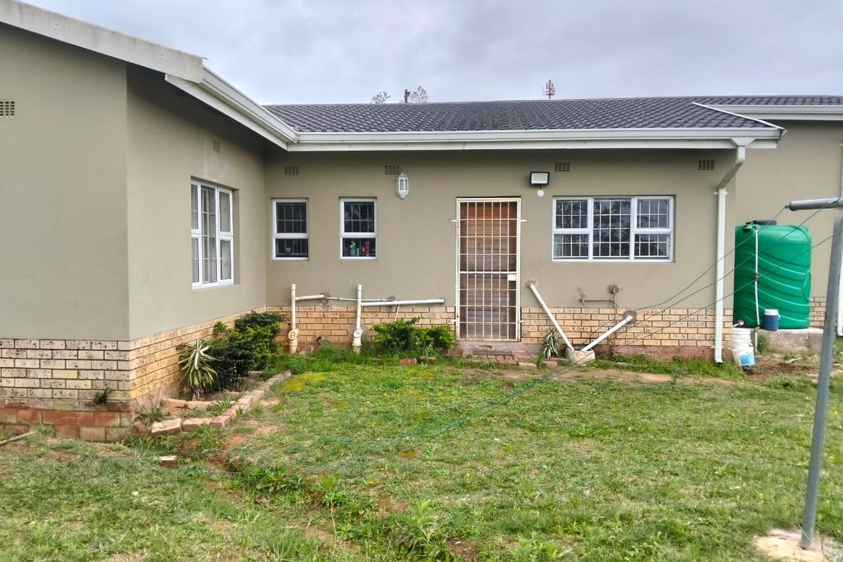Rear view of the property showing the exterior wall, security gate, and water tank installation with surrounding garden area.