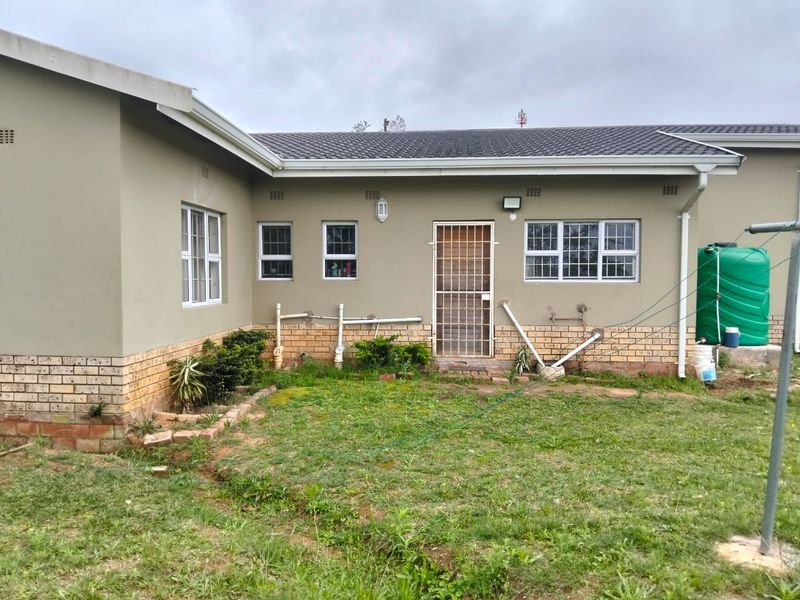 Rear view of the property showing the exterior wall, security gate, and water tank installation with surrounding garden area.