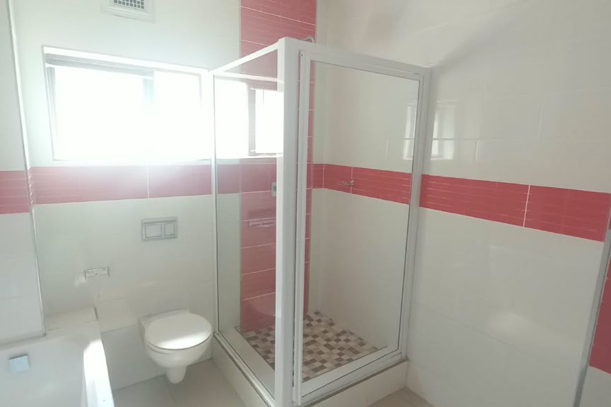 A clean, functional bathroom featuring a bathtub, separate shower enclosure, and wall-mounted toilet with decorative red and white tiled wall accents.