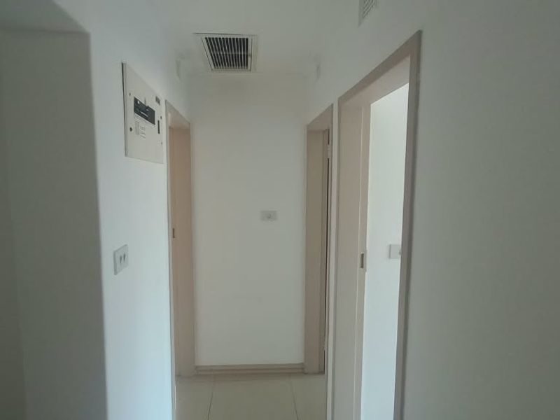 A clean, neutral hallway featuring tiled flooring, built-in electrical distribution board, and integrated ducted air conditioning ventilation.