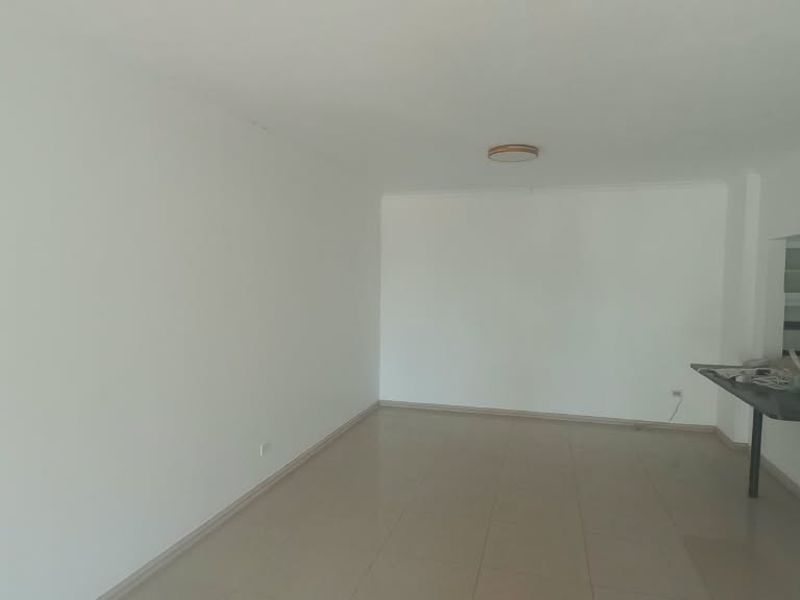 An empty open-plan living and kitchen area featuring tiled flooring and a breakfast bar, offering a blank canvas for interior design.