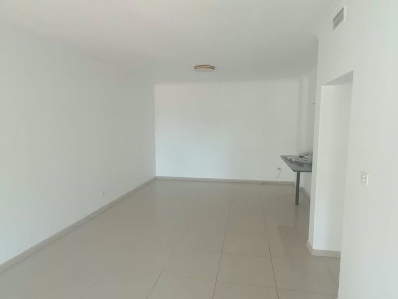 A bright, empty living area featuring neutral tiled flooring, recessed ceiling lighting, and an integrated air conditioning vent.