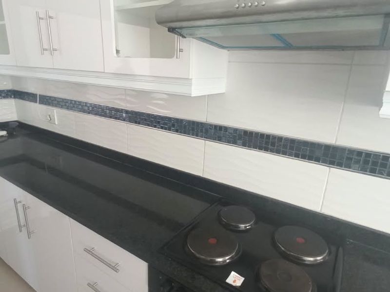 Modern kitchen featuring sleek white cabinetry, dark granite countertops, a built-in electric hob, and a stylish tiled backsplash.