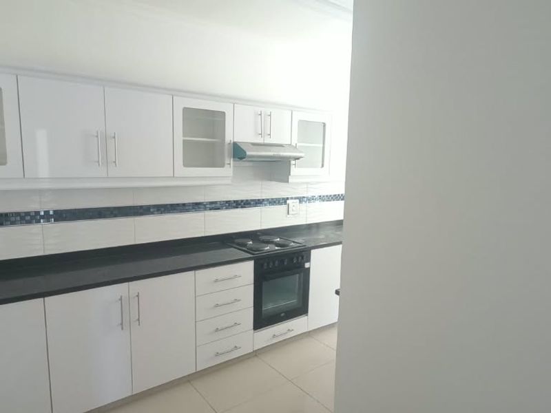 A clean, modern kitchen featuring white cabinetry, black granite countertops, built-in oven, electric hob, and a tiled backsplash.