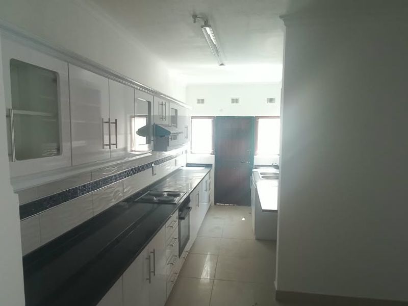 A functional kitchen featuring white cabinetry, dark granite countertops, built-in oven and hob, and tiled flooring, offering a clean and practical workspace.