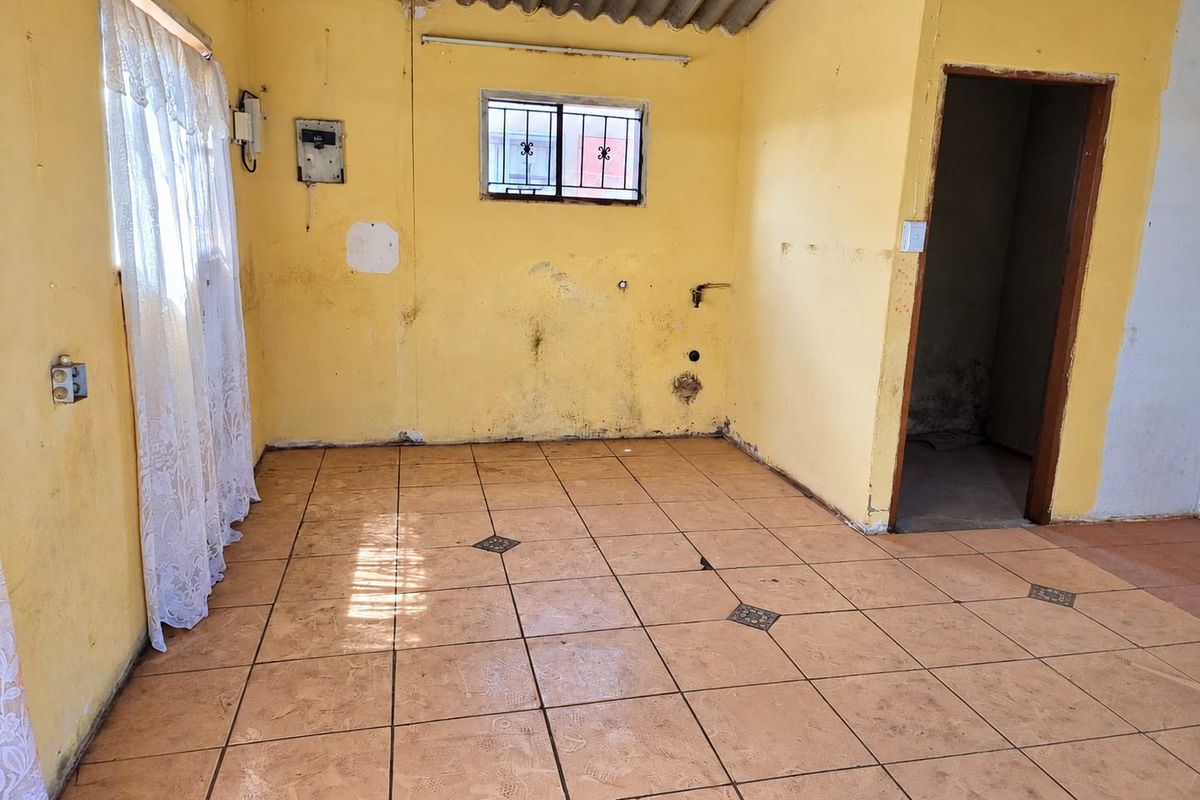 An empty kitchen space featuring tiled flooring, exposed ceiling, and existing plumbing connections, requiring renovation and cosmetic updates to restore functionality.