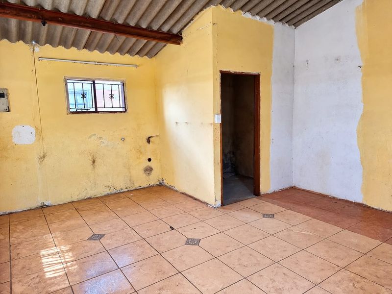 An empty living area featuring tiled flooring, exposed roof structure, and security bars on the window, requiring significant cosmetic renovation and wall repairs.