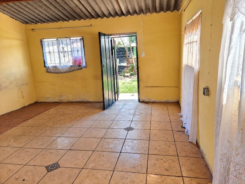 An empty living area featuring tiled floors, security bars on windows, and a corrugated roof, requiring cosmetic updates and wall repairs.