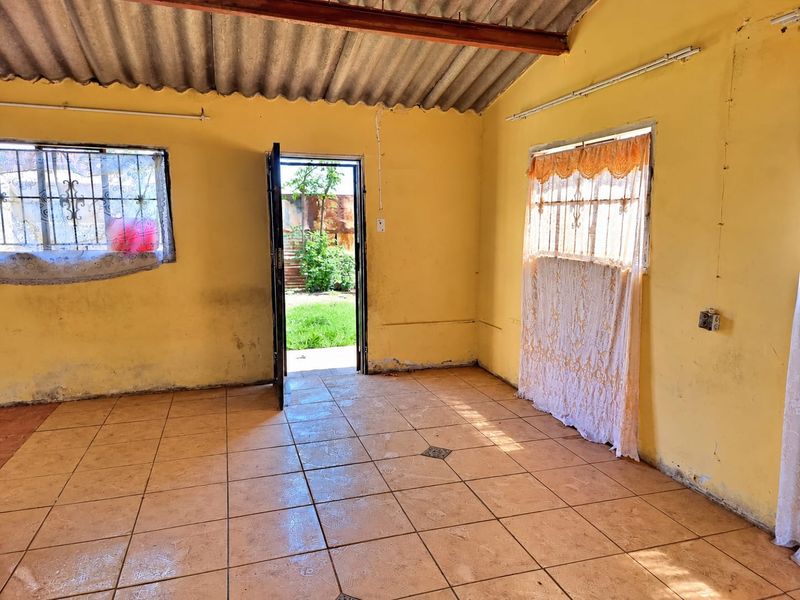 An empty living area featuring tiled floors, exposed beam ceiling, and direct access to the rear garden through an external door.