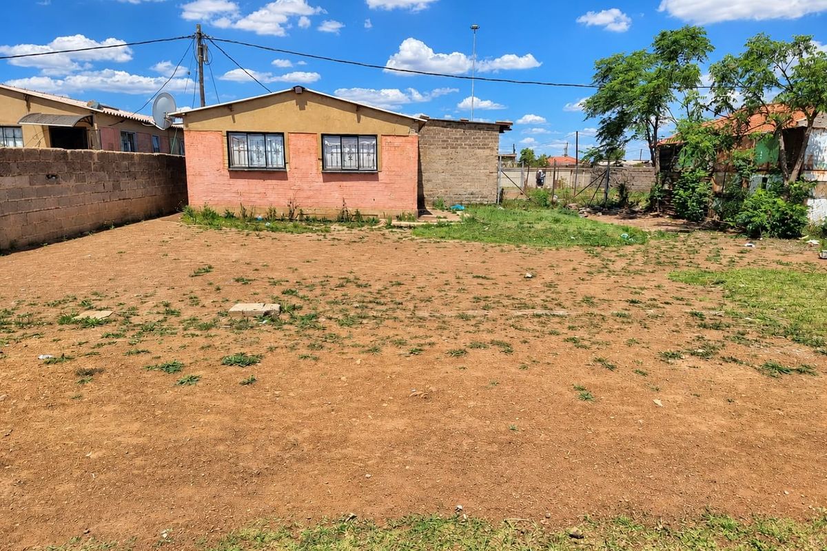 Rear view of the property featuring a large open yard area with a brick boundary wall and a single-story residential structure.