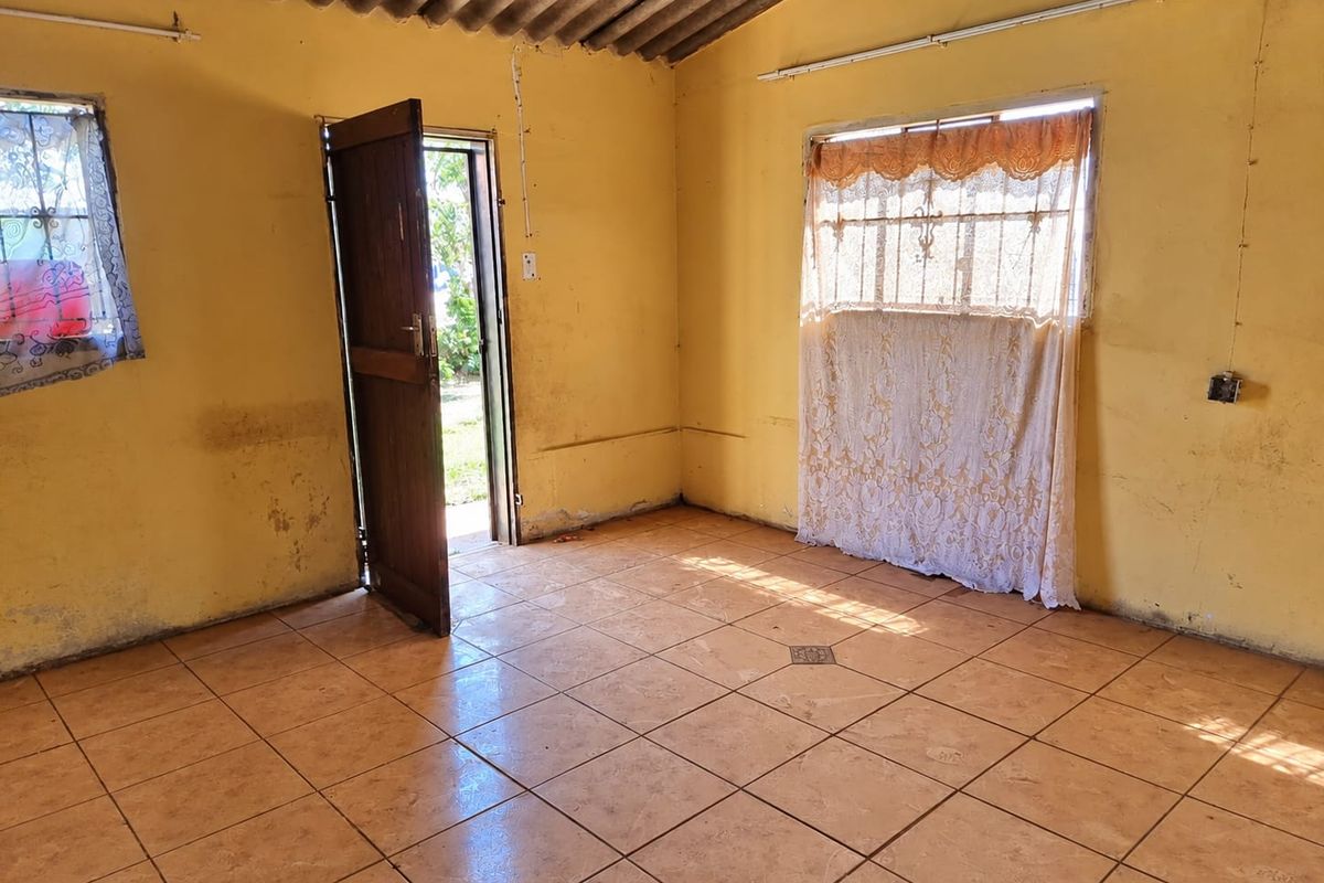 An empty living area featuring tiled flooring, exposed corrugated roofing, and direct access to the exterior through a timber door.
