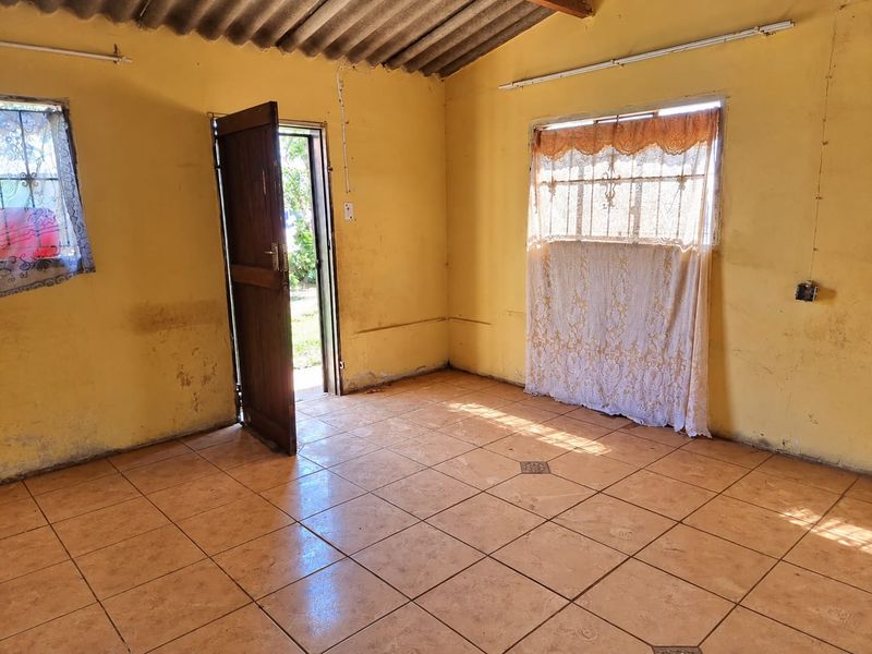 An empty living area featuring tiled flooring, exposed corrugated roofing, and direct access to the exterior through a timber door.