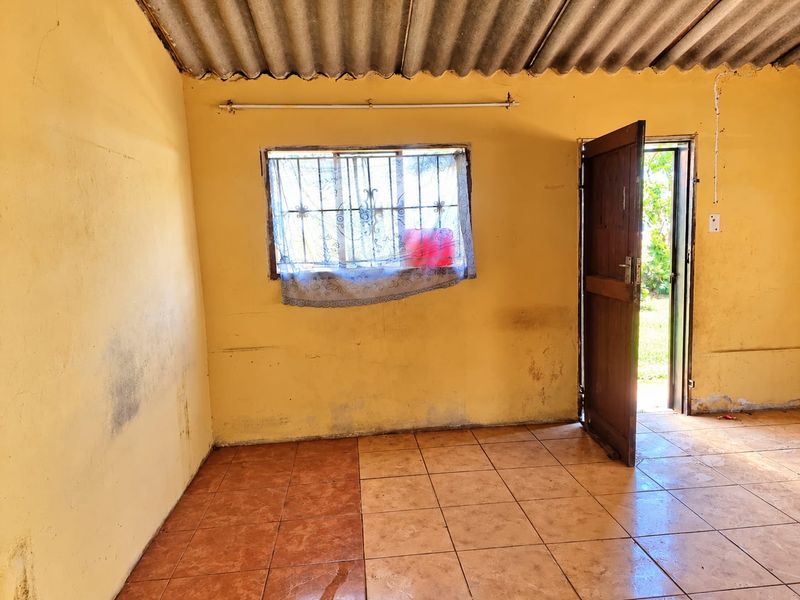 An empty living area featuring tiled flooring, security bars on the window, and direct access to the exterior through a timber door.
