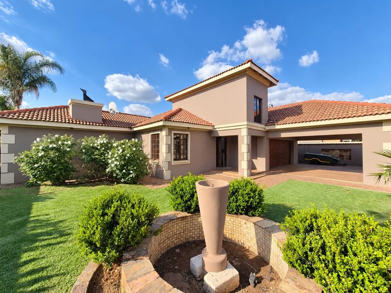 A well-maintained single-story residence featuring a terracotta tiled roof, paved driveway, double garage, and a landscaped front garden with a central water feature.
