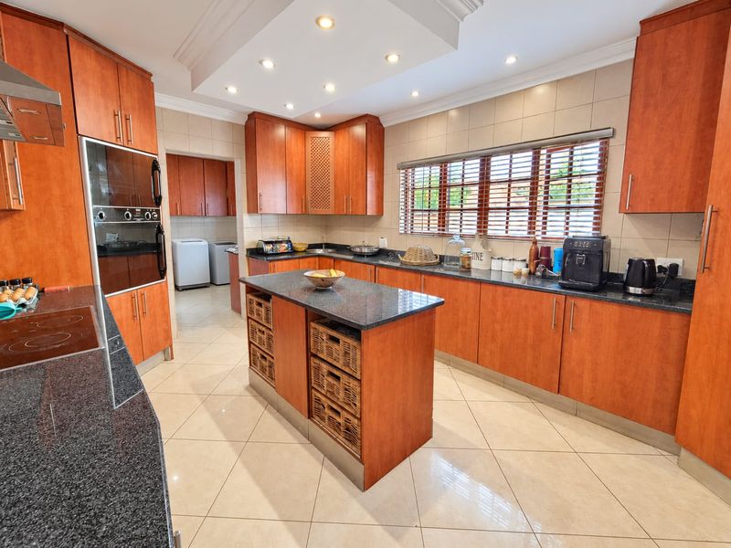Spacious kitchen featuring warm-toned wooden cabinetry, granite countertops, a central island, and integrated appliances, with a convenient adjoining scullery area.