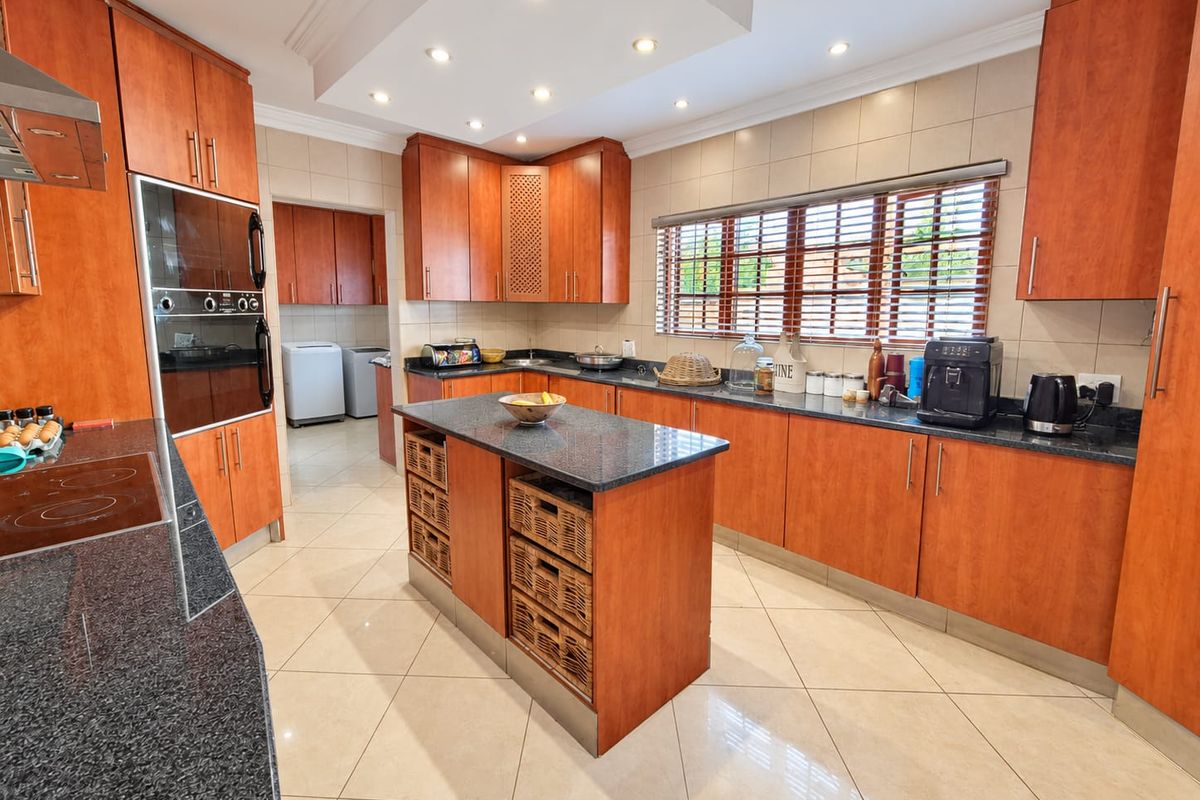 Spacious kitchen featuring warm-toned wooden cabinetry, granite countertops, a central island, and integrated appliances, with a convenient adjoining scullery area.