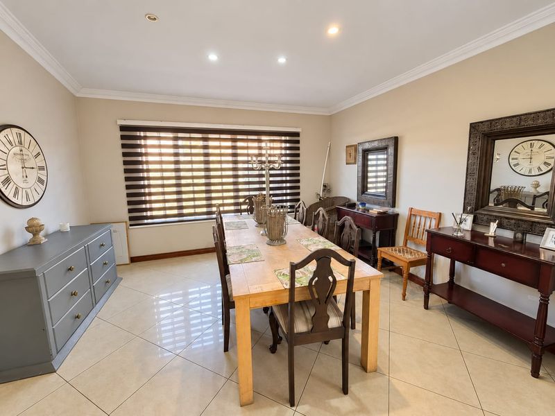 A well-maintained dining room featuring neutral tiled flooring, recessed downlighting, coved cornicing, and modern roller blinds.
