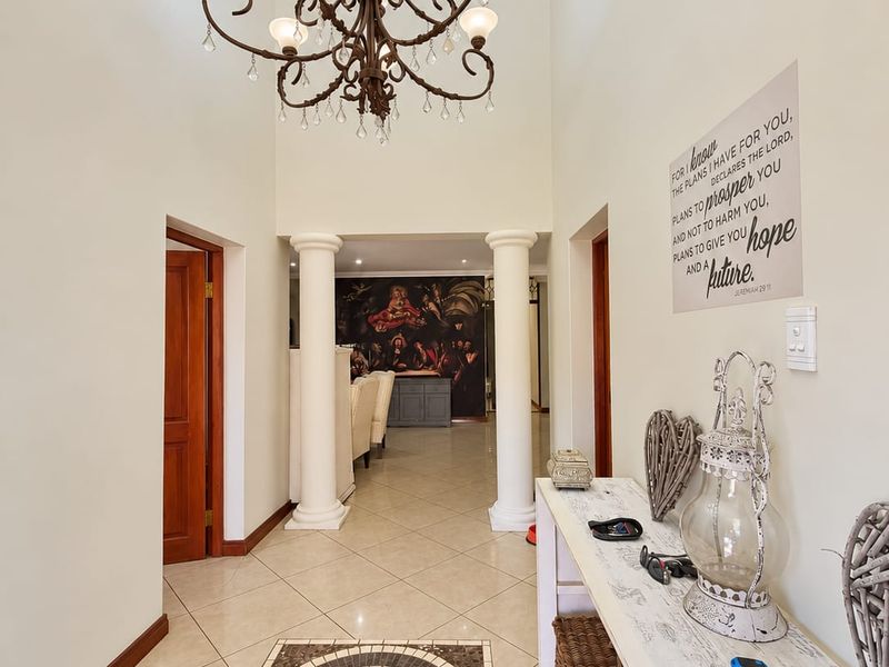 Spacious entrance hall featuring high ceilings, a grand chandelier, decorative columns, and elegant tiled flooring with a central mosaic inlay.