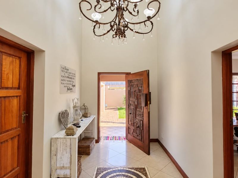 Welcoming entrance hall featuring high ceilings, a decorative chandelier, tiled flooring with a central mosaic inlay, and a solid wood front door.