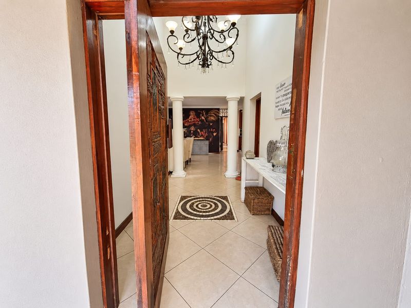 Welcoming entrance hall featuring an ornate wooden door, decorative chandelier, and classic columns leading into the main living area.