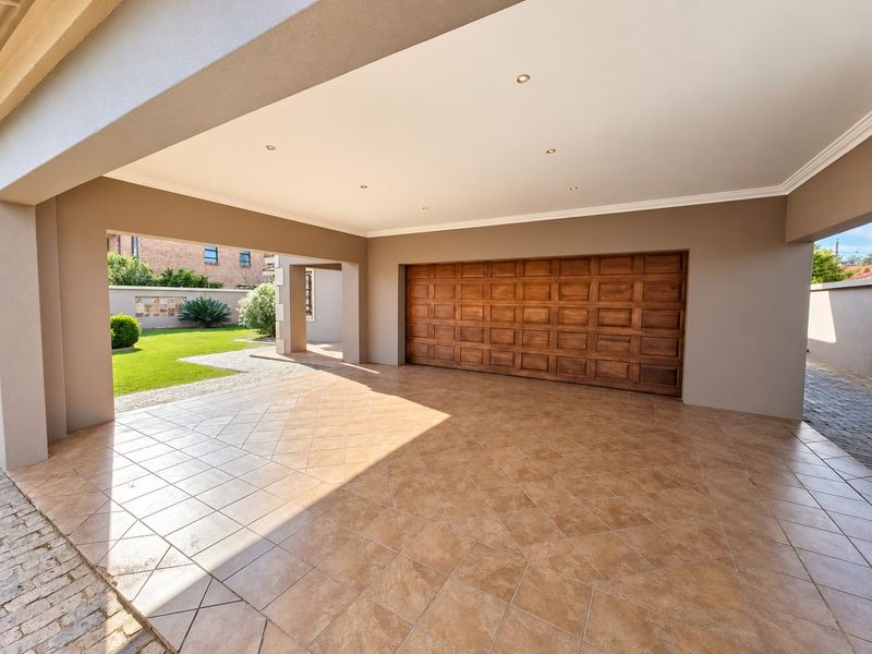 A spacious, well-maintained covered garage area featuring tiled flooring, recessed lighting, and a large wooden sectional door with direct access to the garden.