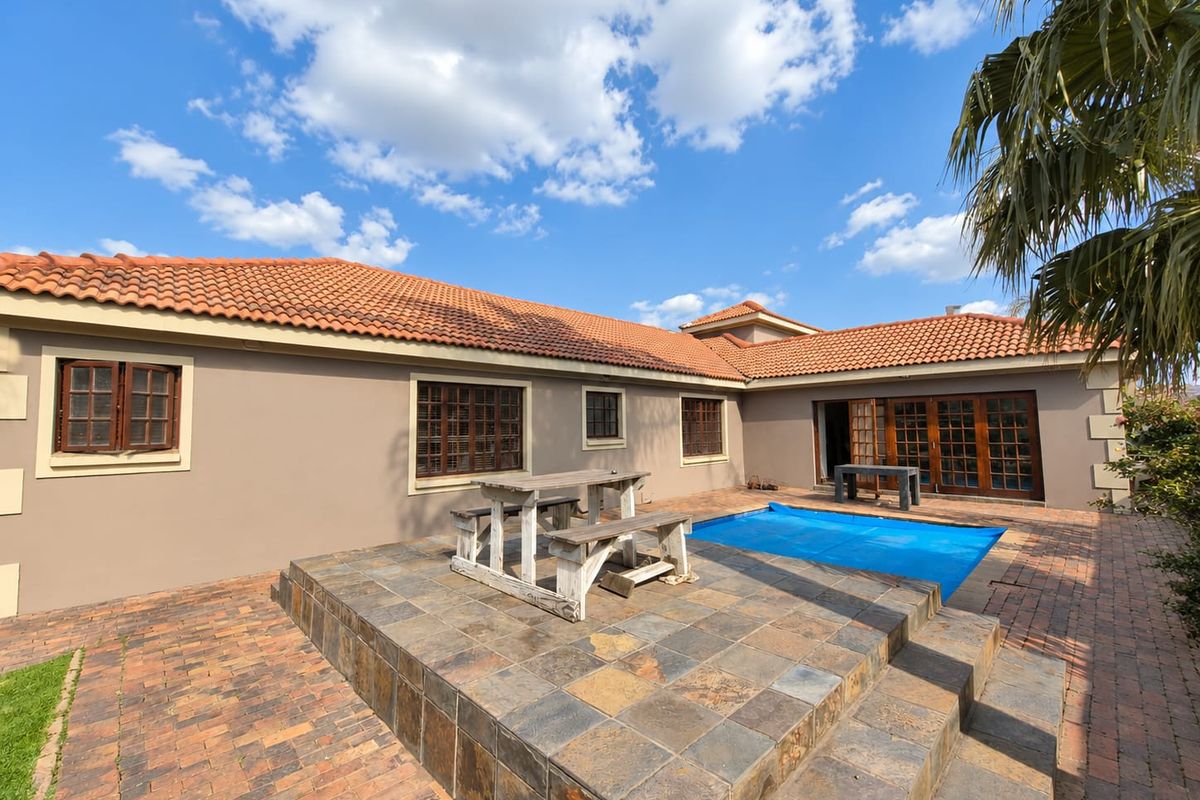 Rear exterior view featuring a raised tiled patio, swimming pool with cover, and brick-paved garden area with timber-framed windows and doors.