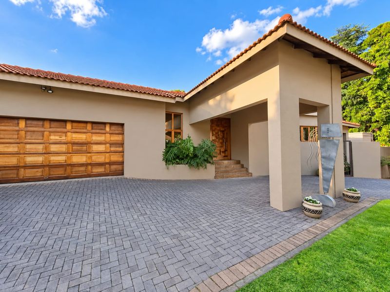 Front elevation of a well-maintained house featuring a paved driveway, covered entrance, and a wooden garage door.