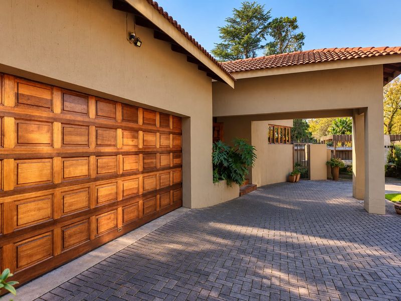 Front exterior view featuring a paved driveway, covered entrance, and a well-maintained wooden sectional garage door under a terracotta tiled roof.