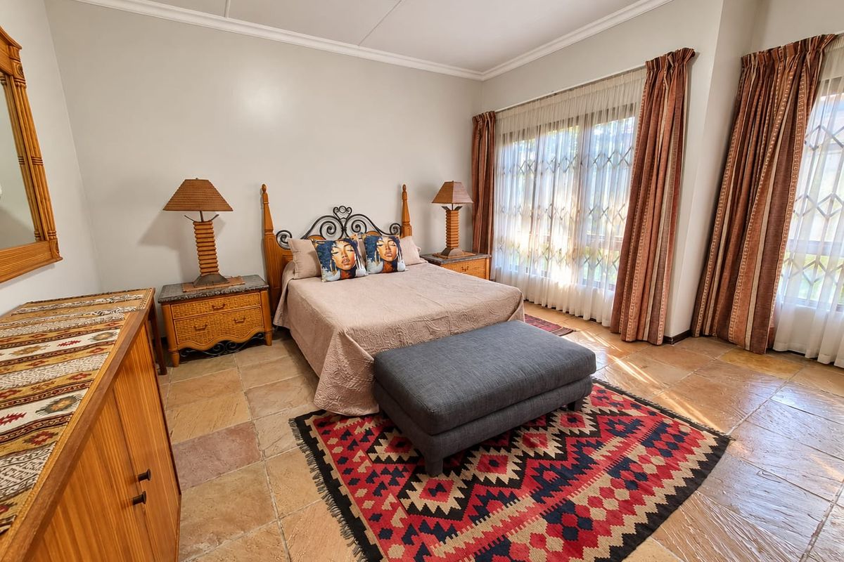 A spacious bedroom featuring natural stone tile flooring, large windows with security gates, and coved ceiling detailing.