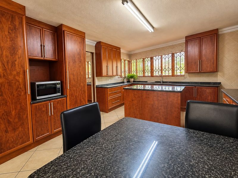 Spacious kitchen featuring warm-toned wooden cabinetry, granite countertops, a central island, and tiled flooring, offering a functional and well-maintained cooking space.