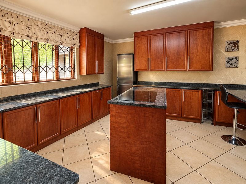 A well-maintained kitchen featuring warm-toned wooden cabinetry, granite countertops, a central island with an integrated hob, and neutral tiled flooring.