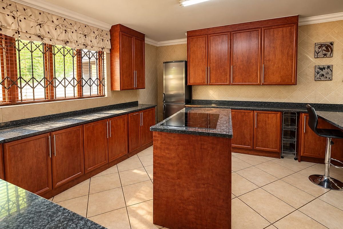 A well-maintained kitchen featuring warm-toned wooden cabinetry, granite countertops, a central island with an integrated hob, and neutral tiled flooring.