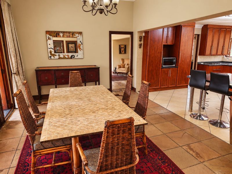 Open-plan dining area seamlessly connected to a kitchen featuring warm-toned wooden cabinetry, tiled flooring, and a central island with breakfast bar seating.