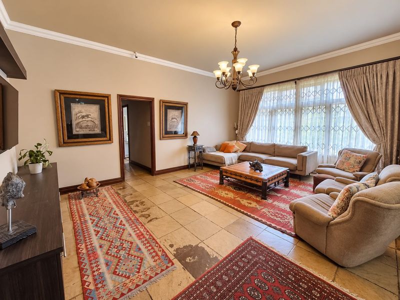 Spacious living room featuring stone tile flooring, crown molding, and a classic chandelier, offering a comfortable and traditional living space.