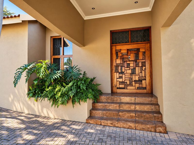 A well-maintained front entrance featuring a unique custom wooden door, tiled steps, and a built-in planter box under a covered porch area.