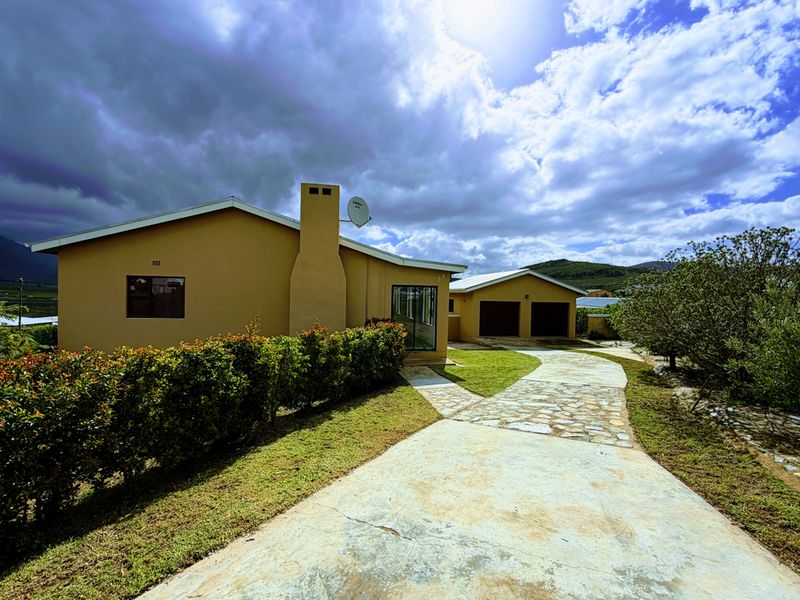 Front exterior view of a single-story house featuring a paved driveway, stone walkway, chimney, and a detached double garage.