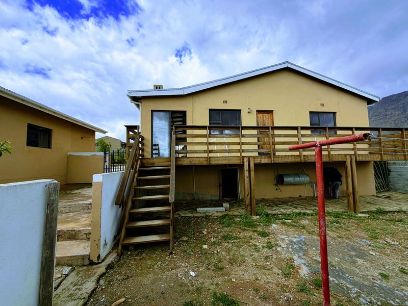 Rear view of the house featuring a raised wooden deck, external staircase, and a paved patio area with an external geyser.