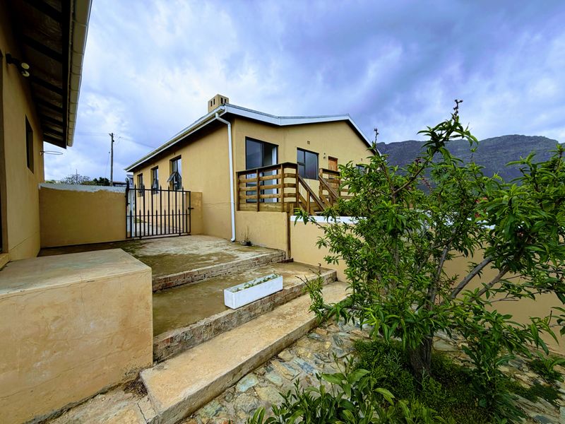 Rear exterior view of the house featuring a timber deck, concrete stairs, and a stone-paved garden area with mountain views.