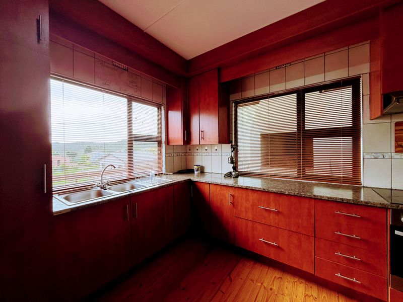 A functional kitchen featuring warm-toned wooden cabinetry, granite countertops, a double basin sink, and timber flooring, offering a classic and practical workspace.