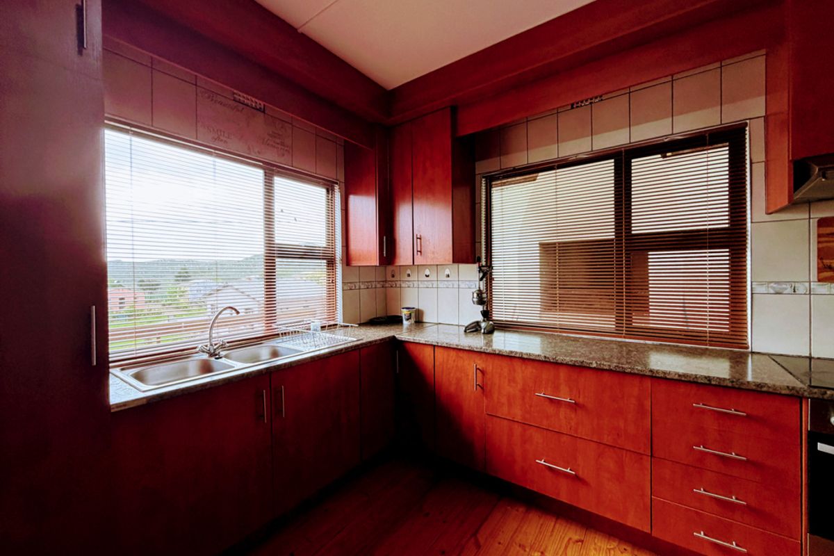A functional kitchen featuring warm-toned wooden cabinetry, granite countertops, a double basin sink, and timber flooring, offering a classic and practical workspace.