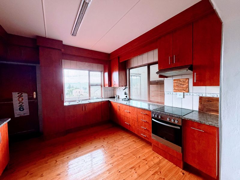 A functional kitchen featuring warm-toned wooden cabinetry, granite countertops, integrated oven and hob, and polished wooden flooring with ample natural light.