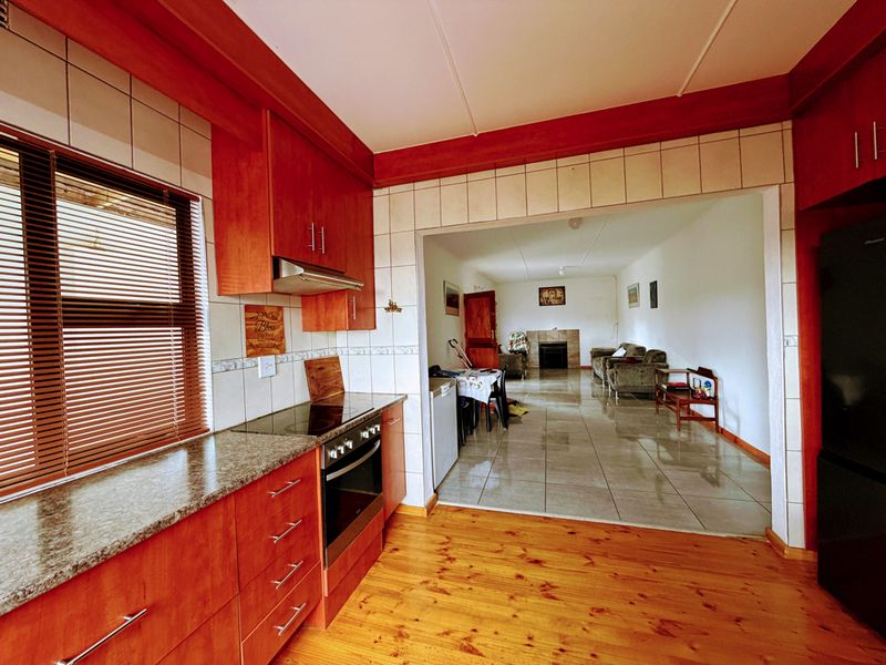 Open-plan kitchen and living area featuring timber and tiled flooring, granite countertops, built-in cabinetry, and a fireplace in the adjacent lounge space.
