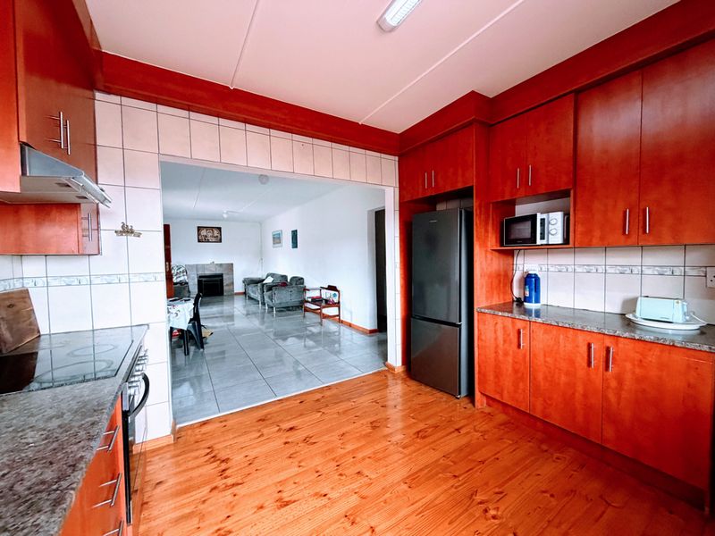 Open-plan kitchen and living area featuring wooden cabinetry, granite countertops, and a mix of tiled and wooden flooring, creating a functional living space.
