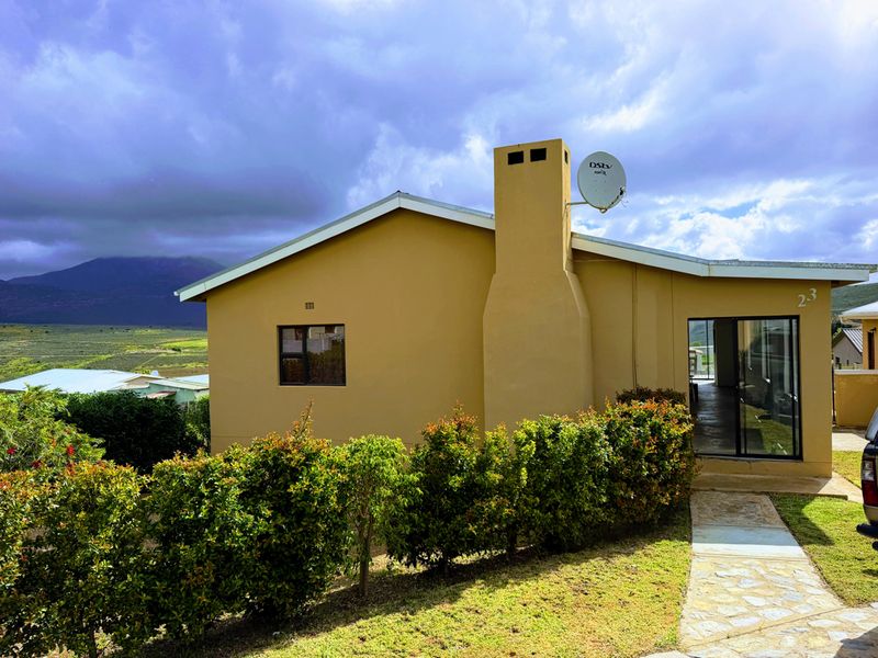 Rear view of the house featuring a chimney, sliding glass door access, and a paved walkway surrounded by landscaped hedges.
