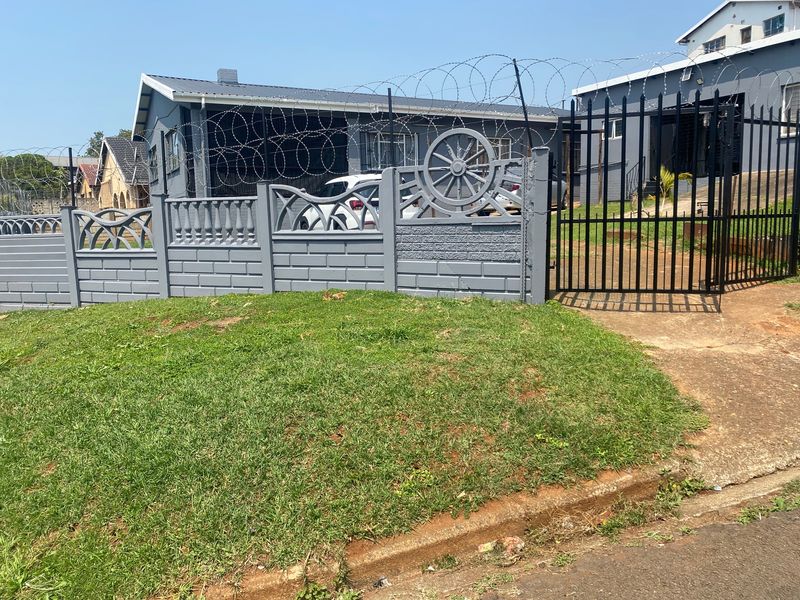 Front exterior view of the property featuring a secure precast concrete boundary wall with razor wire and a metal driveway gate.