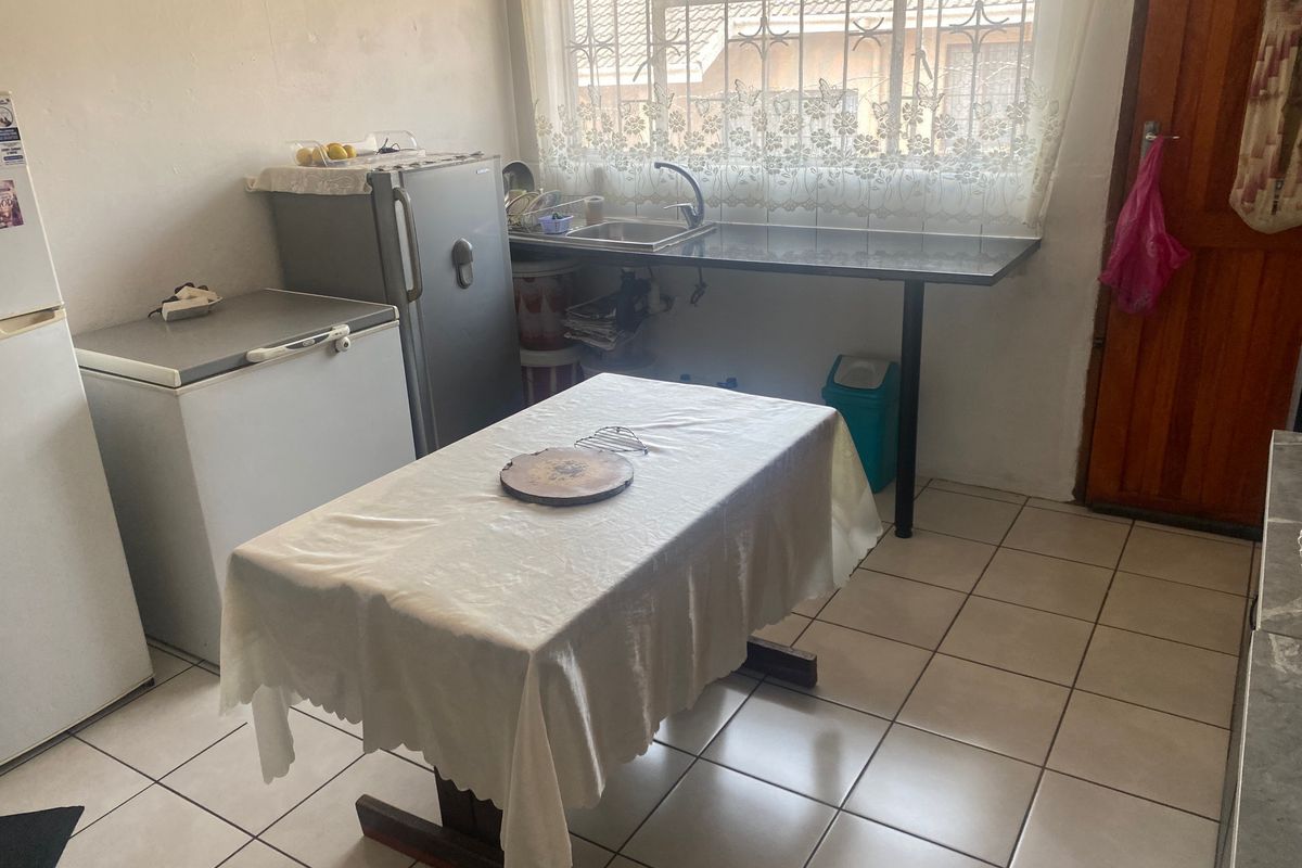 A functional kitchen area featuring tiled flooring, a stainless steel sink, and a window with security bars.
