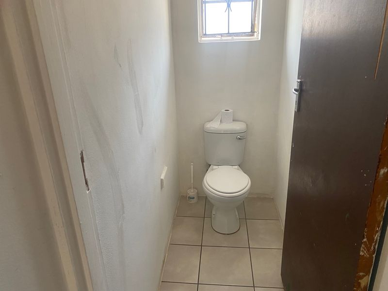 A small, functional guest toilet featuring tiled flooring and a window, currently requiring cosmetic updates to the walls and door frame.