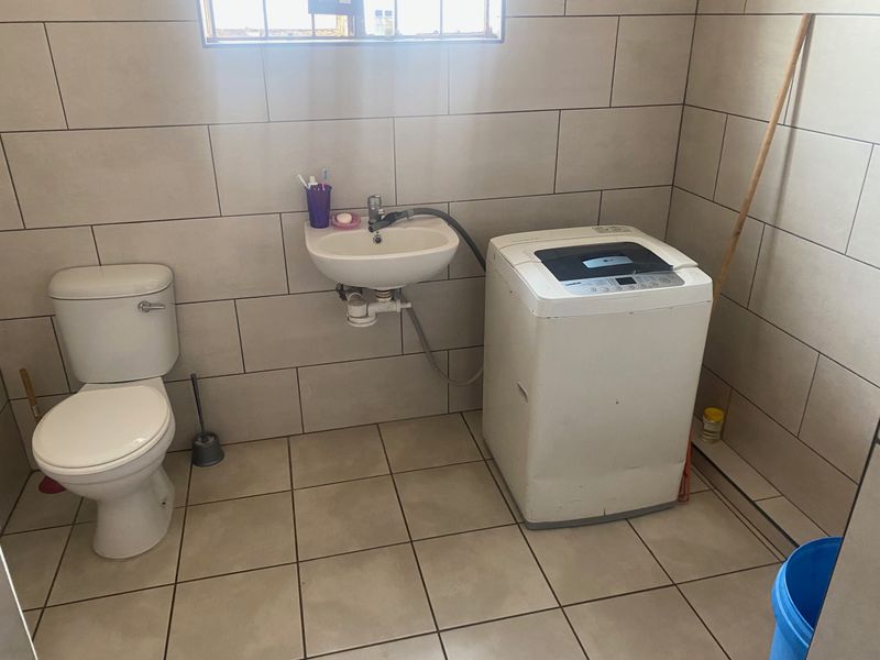 A functional laundry room featuring tiled walls and flooring, equipped with a toilet and a wall-mounted basin.